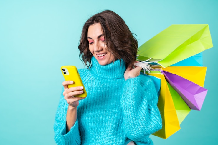 Foto gratuito acogedor retrato de una mujer joven con un suéter azul tejido y maquillaje rosa brillante con bolsas de la compra y un teléfono móvil