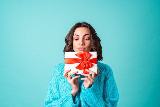 Acogedor retrato de una mujer joven con un suéter azul tejido y maquillaje rosa brillante sosteniendo una caja de regalo