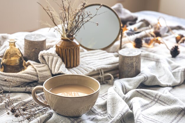 Acogedora composición otoñal con una taza de café y velas en la cama