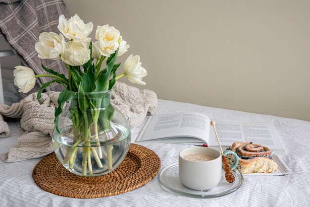 Acogedora composición con un ramo de flores, café y un bollo en la cama.