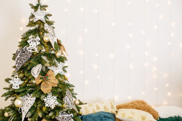 Una acogedora habitación decorada con guirnaldas y árboles de navidad. la cama tipo almohada blanca es elegante y moderna. buen espíritu de año nuevo. lugar de textura de fondo de colores claros para el texto. decoración de dormitorio para las vacaciones. Foto Premium 