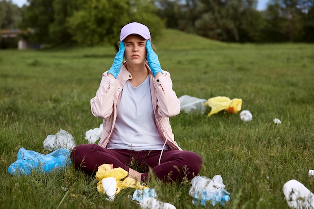 Foto gratuita activista ambiental cansado sentado en la hierba verde con los dedos en las sienes