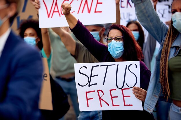 Activista femenina con mascarilla protectora mientras protesta con un grupo de personas y apoya el movimiento contra la vacunación