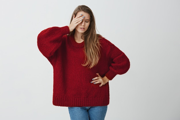 La actriz se está muriendo en mí. Retrato de encantadora estudiante en suéter holgado de moda con la palma de la mano en la frente y mirando a un lado estar en el papel, jugando en el club de teatro, de pie