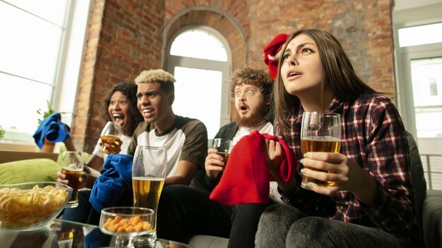 Adentro. Gente emocionada viendo partido deportivo, campeonato en casa. Grupo multiétnico de amigos.