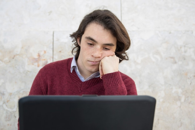 Adolescente aburrido usando una computadora portátil al aire libre