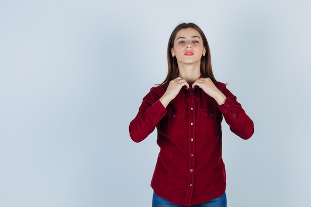 Foto gratuita adolescente ajustando el cuello de la camisa en camisa burdeos y mirando confiado, vista frontal.