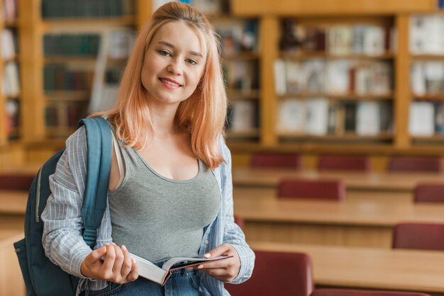 Adolescente alegre cerca de mesas de la biblioteca