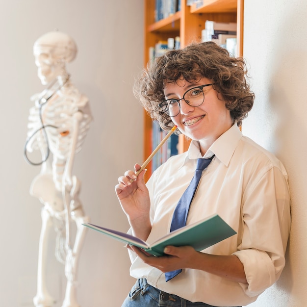 Foto gratuita adolescente alegre con lápiz y cuaderno en biblioteca