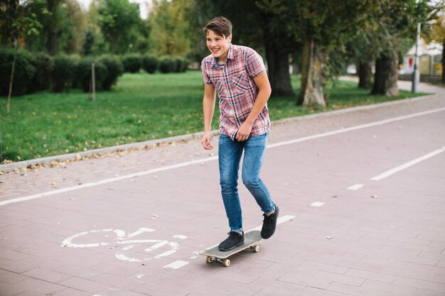 Adolescente alegre que anda en monopatín cerca del carril de la bici
