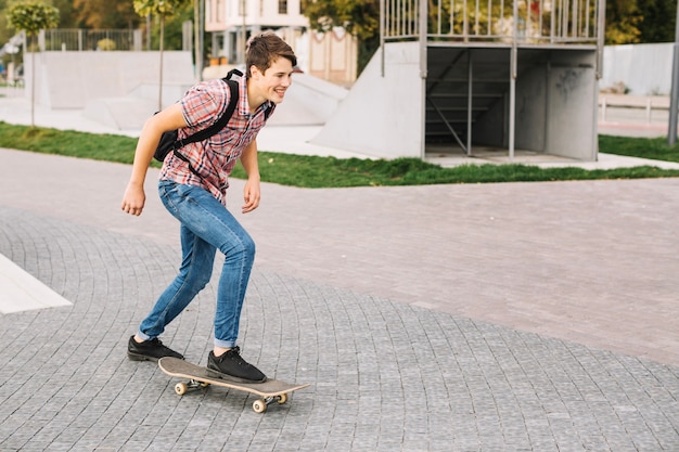 Adolescente alegre que anda en monopatín en parque