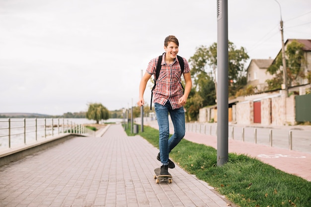 Adolescente alegre que anda en monopatín en el pavimento