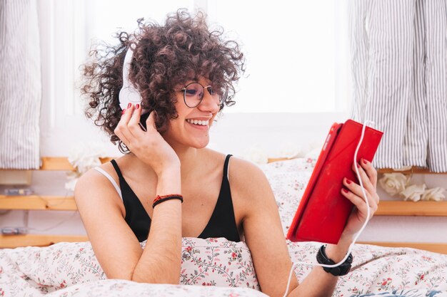 Foto gratuita adolescente alegre en tableta de navegación de auriculares en la cama