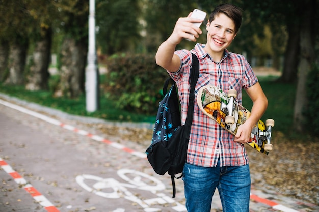 Adolescente alegre tomando selfie con patín