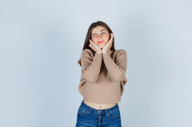 Adolescente almohada cara en sus manos en suéter, jeans y mirando pensativo. vista frontal.