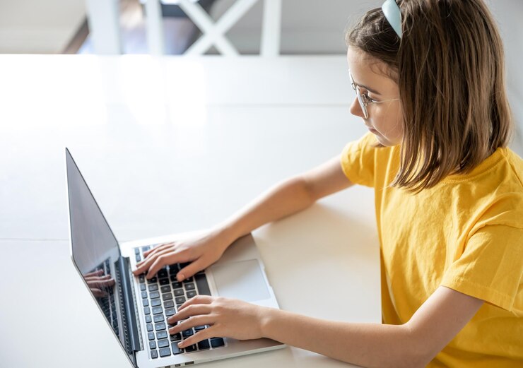 Foto gratuito una adolescente con anteojos usa una computadora portátil mientras se sienta en una mesa en casa