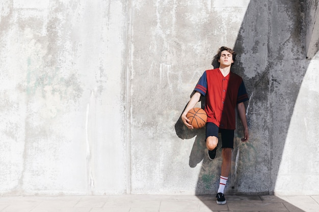 Adolescente apoyado en la pared con baloncesto