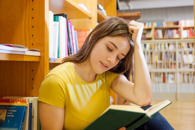 Foto gratuita adolescente apoyando la cabeza y leyendo en la biblioteca