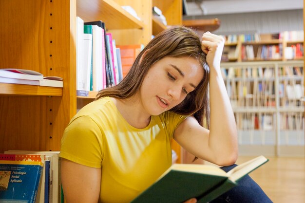 Adolescente apoyando la cabeza y leyendo en la biblioteca