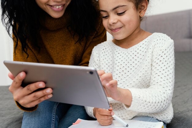 Adolescente ayudando a hermanita con tableta para escuela en línea