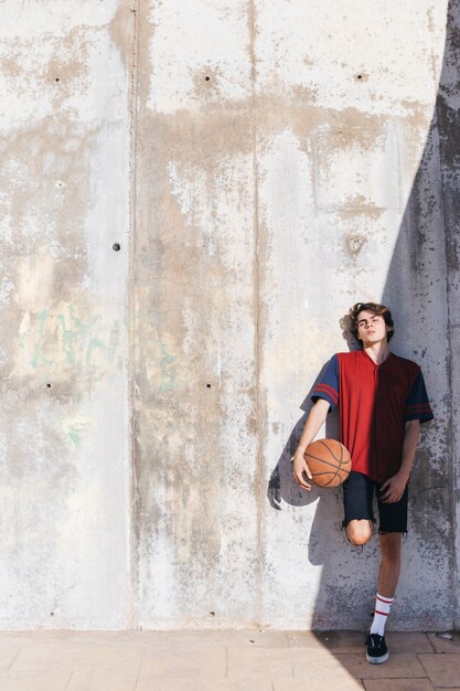 Adolescente con baloncesto apoyado en la pared