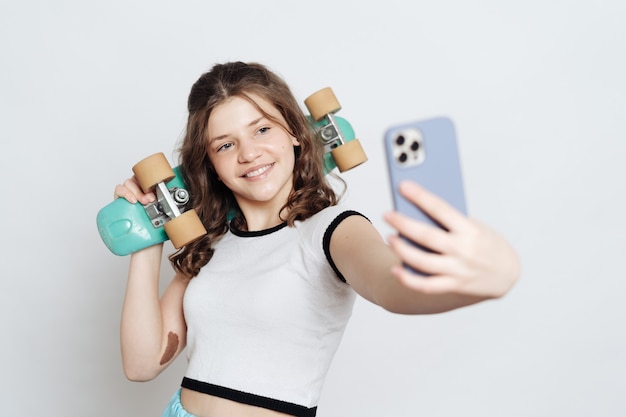 Adolescente chica tomando selfie en teléfono mientras posa con tablero de centavo azul sobre blanco