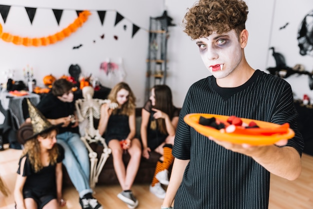 Foto gratuita adolescente con colmillos y vampiro severo dando plato con dulces