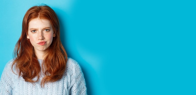 Foto gratuita adolescente decepcionada con el pelo rojo frunciendo el ceño y sonriendo disgustado mirando suplente crítico