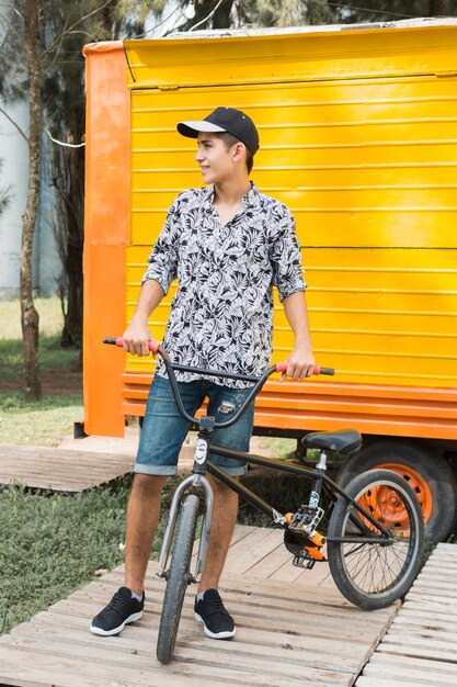 Adolescente elegante sonriente con su bicicleta que mira lejos