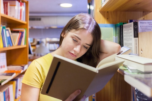 Adolescente encantador leyendo entre estanterías