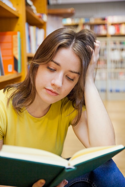 Adolescente enfocado leyendo cerca de librero