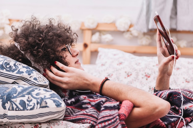 Foto gratuita adolescente escuchando música y navegación por teléfono inteligente en la cama