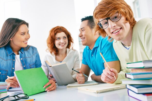 Adolescente feliz sujetando un lápiz con amigos de fondo