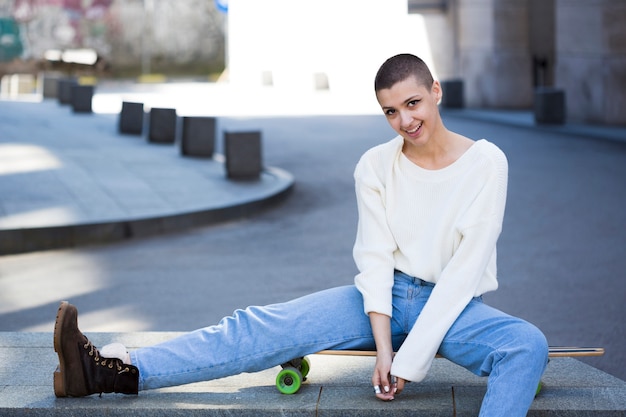 Foto gratuita adolescente femenina con el pelo corto sentado en longboard en la calle