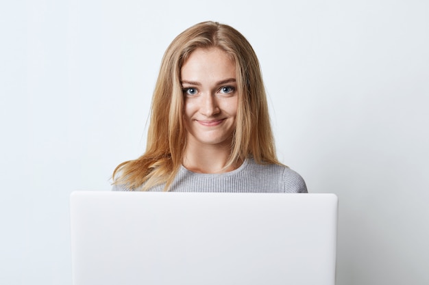 Adolescente femenino que trabaja en la computadora, pre-primavera para las clases o navegar por las redes sociales, mirando con expresión feliz en la cámara aislada en blanco. Modelo femenino con gadget moderno