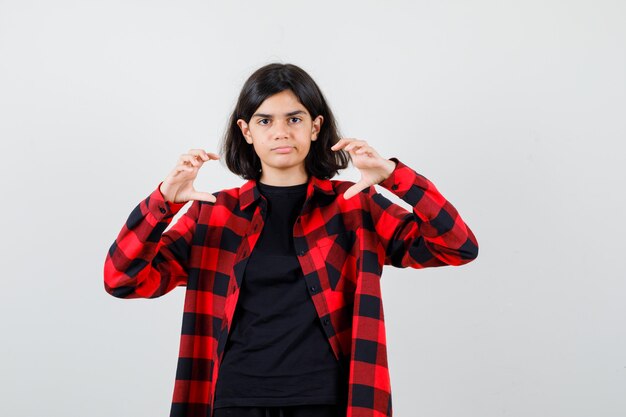 Adolescente fingiendo atrapar algo en camiseta, camisa a cuadros y mirando con cuidado. vista frontal.