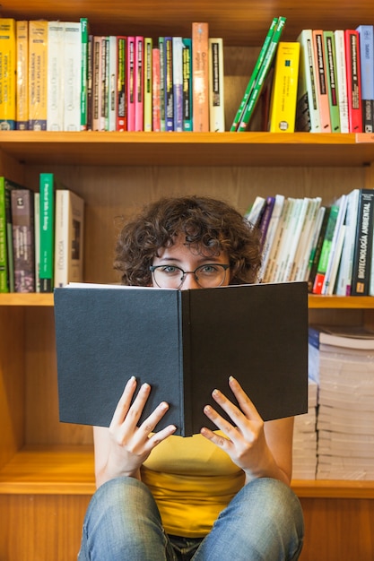 Adolescente en gafas cubriendo la cara con el libro