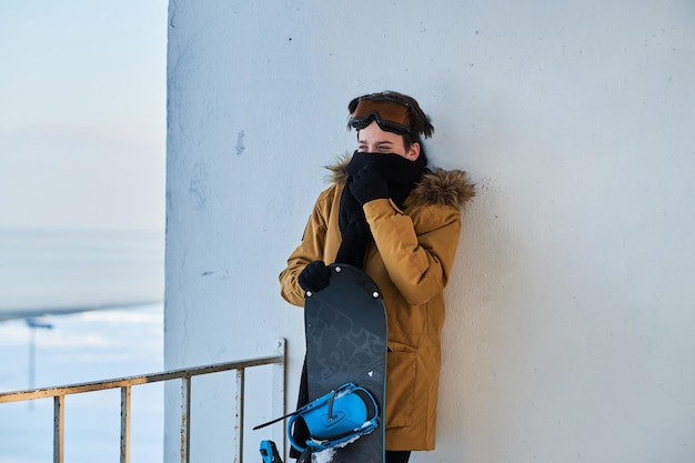 Adolescente con gafas protectoras sostiene su tabla de snowboard mientras posa para el fotógrafo.