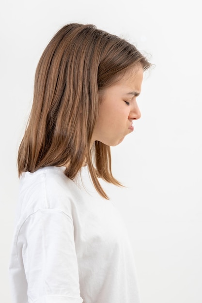 Una adolescente hace caras de descontento en un fondo blanco aislado