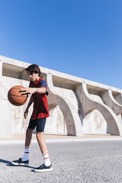 Adolescente jugando al baloncesto contra el cielo azul