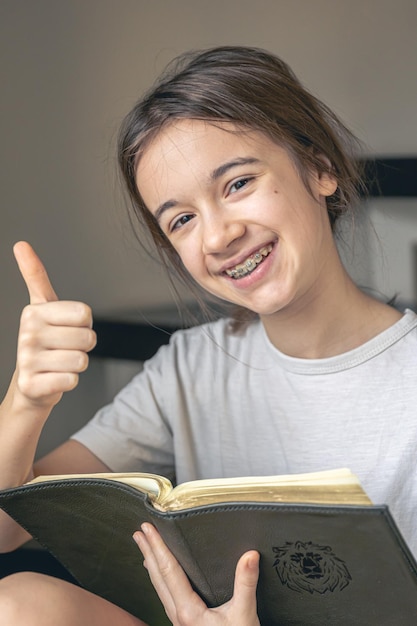 Foto gratuita una adolescente lee un libro y sonríe mostrando sus dientes con aparatos ortopédicos