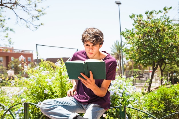 Adolescente leyendo en la cerca en el parque