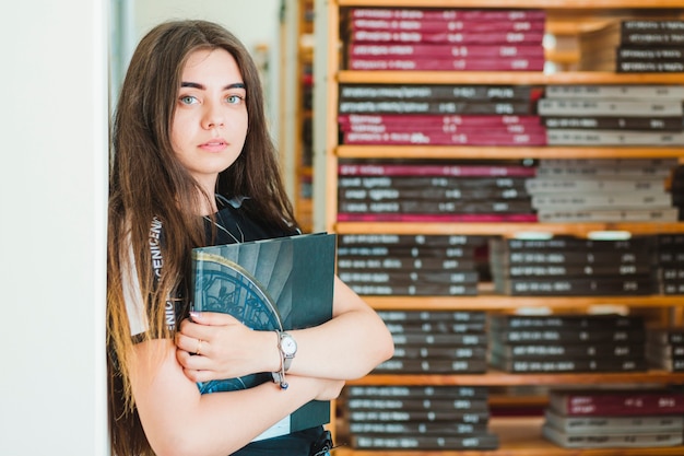 Foto gratuita adolescente con libro apoyado en la pared de la biblioteca