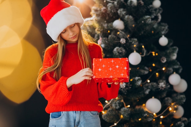 Adolescente linda chica con sombrero rojo de santa por árbol de Navidad
