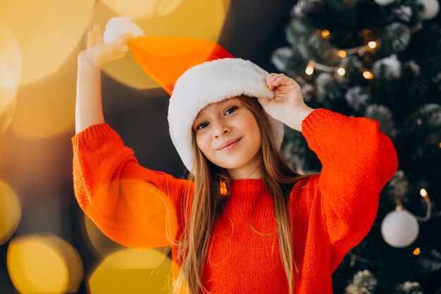 Adolescente linda chica con sombrero rojo de santa por árbol de Navidad