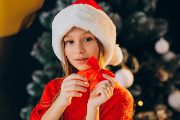 Adolescente linda chica con sombrero rojo de santa por árbol de Navidad