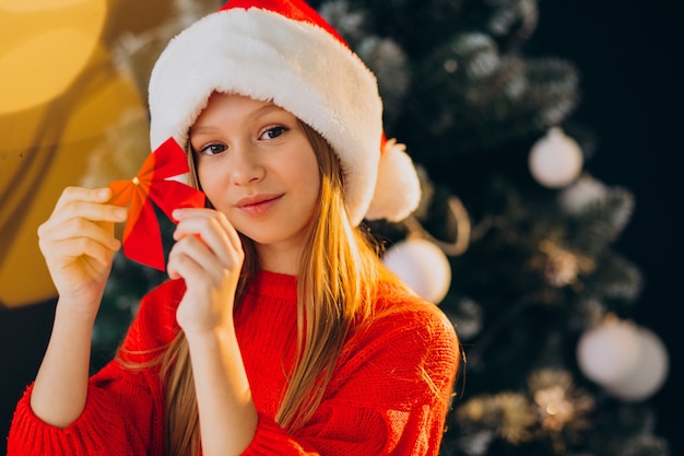 Adolescente linda chica con sombrero rojo de santa por árbol de Navidad