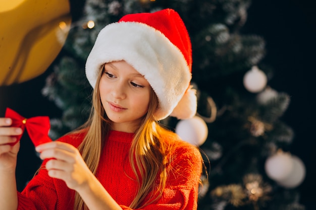 Adolescente linda chica con sombrero rojo de santa por árbol de Navidad