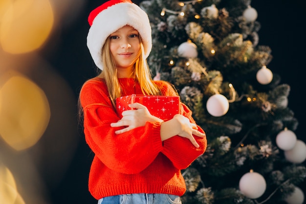 Adolescente linda chica con sombrero rojo de santa por árbol de Navidad