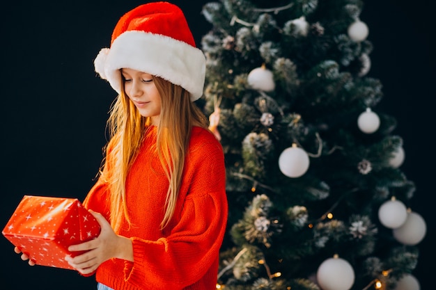 Adolescente linda chica con sombrero rojo de santa por árbol de Navidad